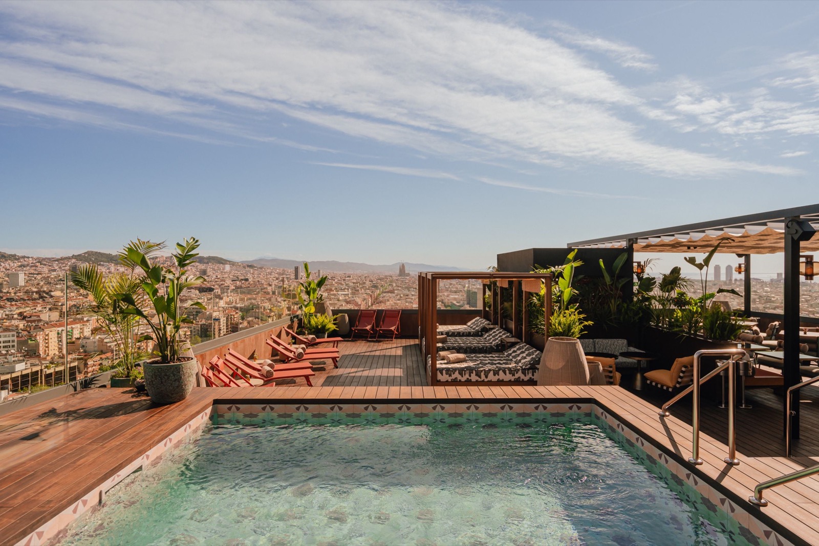 Rooftop pool with cabanas, red loungers and a panoramic Barcelona skyline