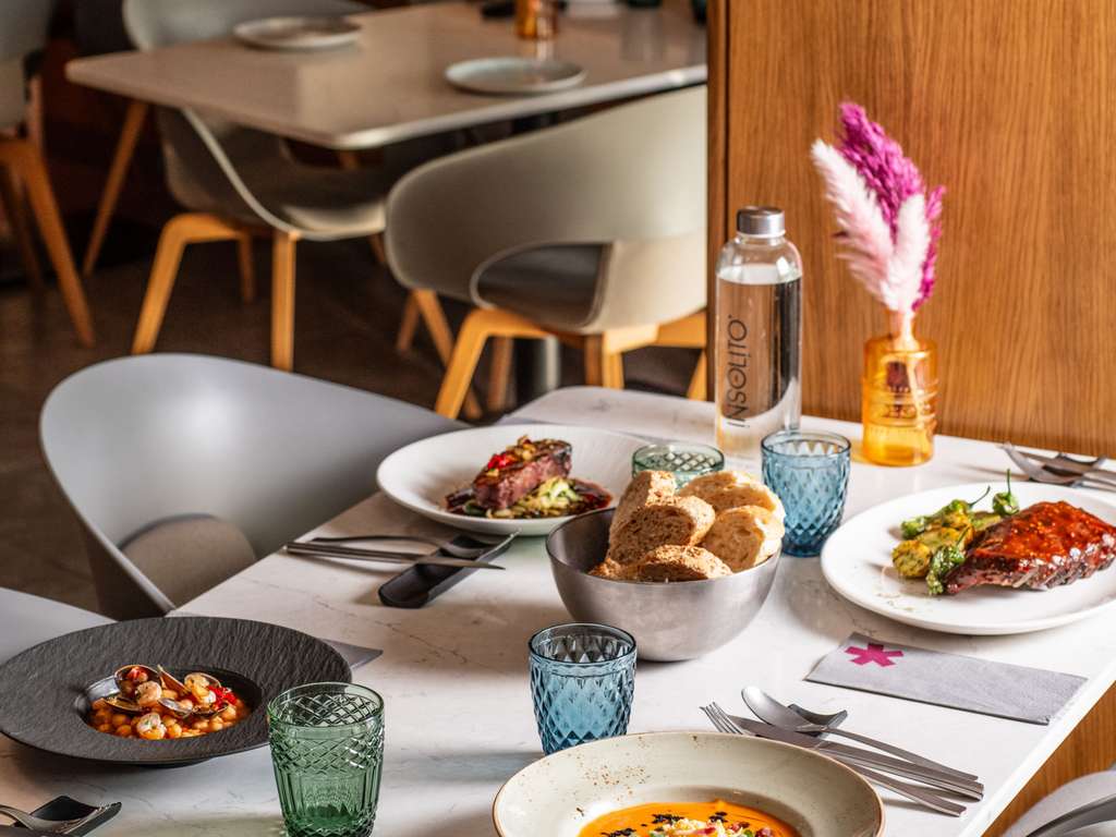 Restaurant table set with grilled meat and seafood dishes, bread, colored glassware and a bottle labeled Insolito.