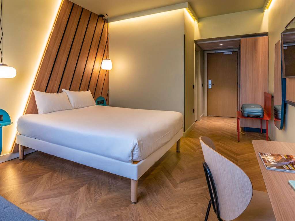 ibis Styles guest room with a white bed against an angled wood-slat headboard and turquoise nightstand accents.