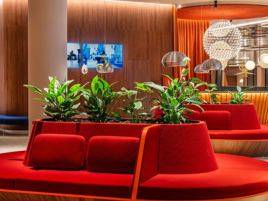 Hotel lobby lounge with curved red banquette seating, potted plants and globe pendant lights.