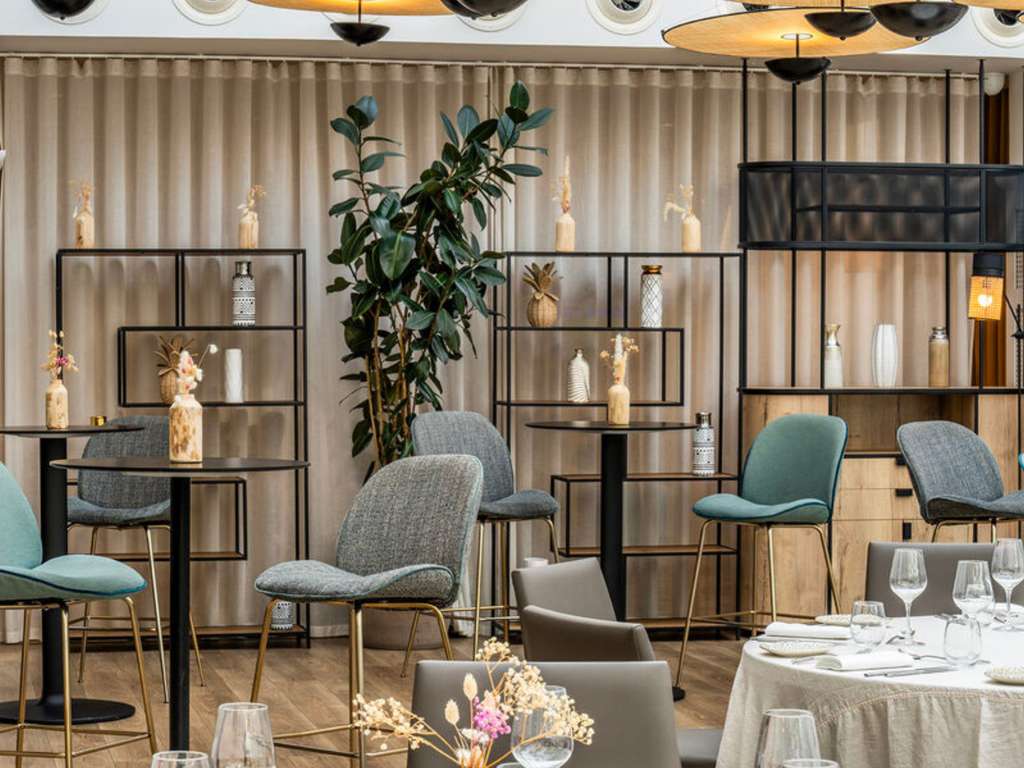Hotel restaurant dining room with small round tables, teal chairs and open shelving decorated with dried flowers.