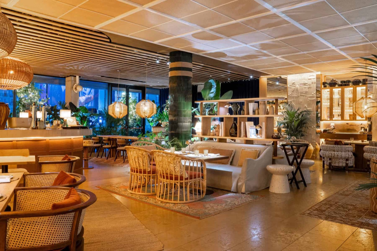 The Mar Mía dining room with rattan chairs, a low sofa, potted plants, a green tiled column and shelving stocked with glassware and bottles.