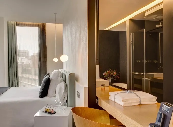 Junior suite with a city-view window, pendant lights and a marble bathroom beyond