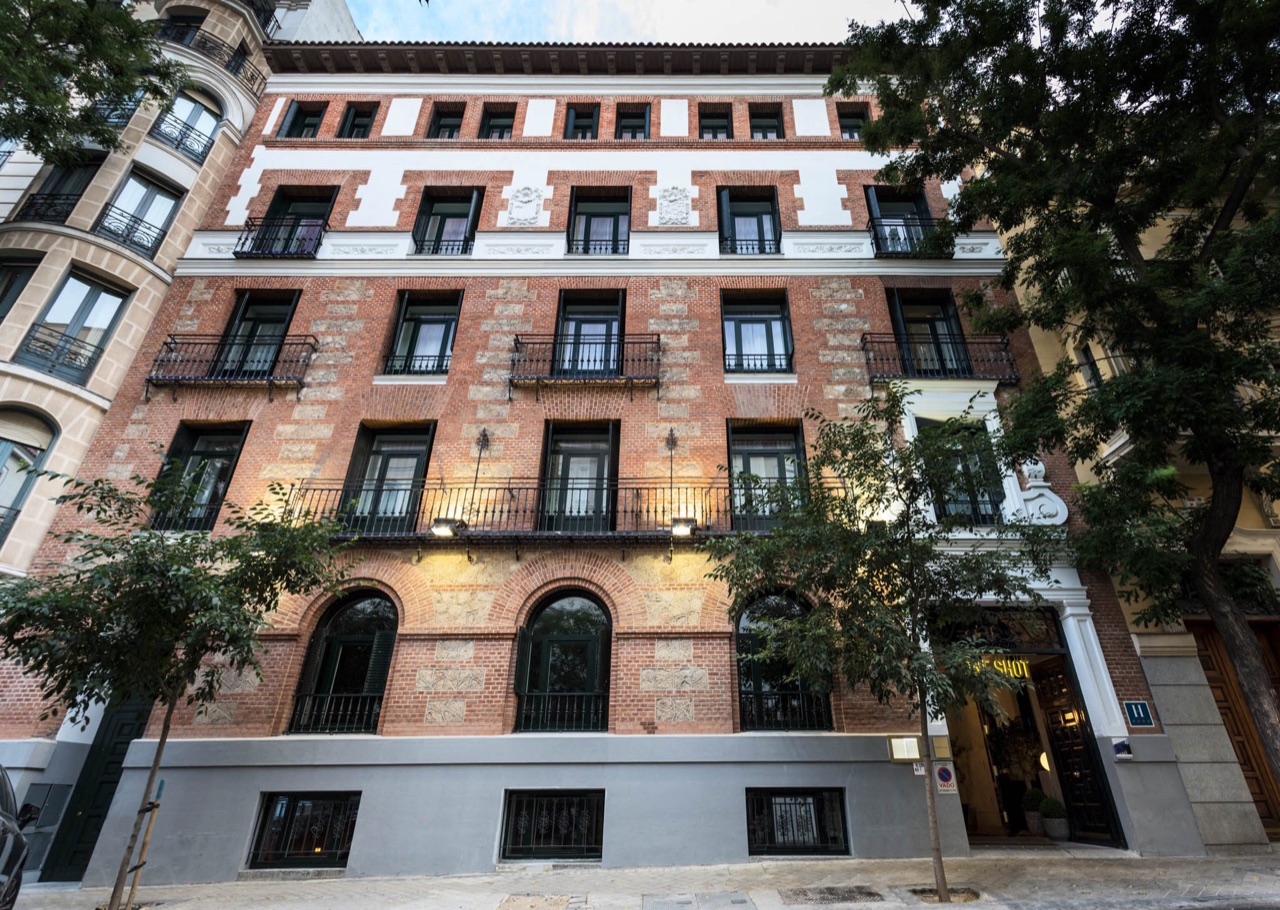 The hotel's red-brick and white-trimmed 1913 facade on a tree-lined street, with the illuminated One Shot sign over the entrance.