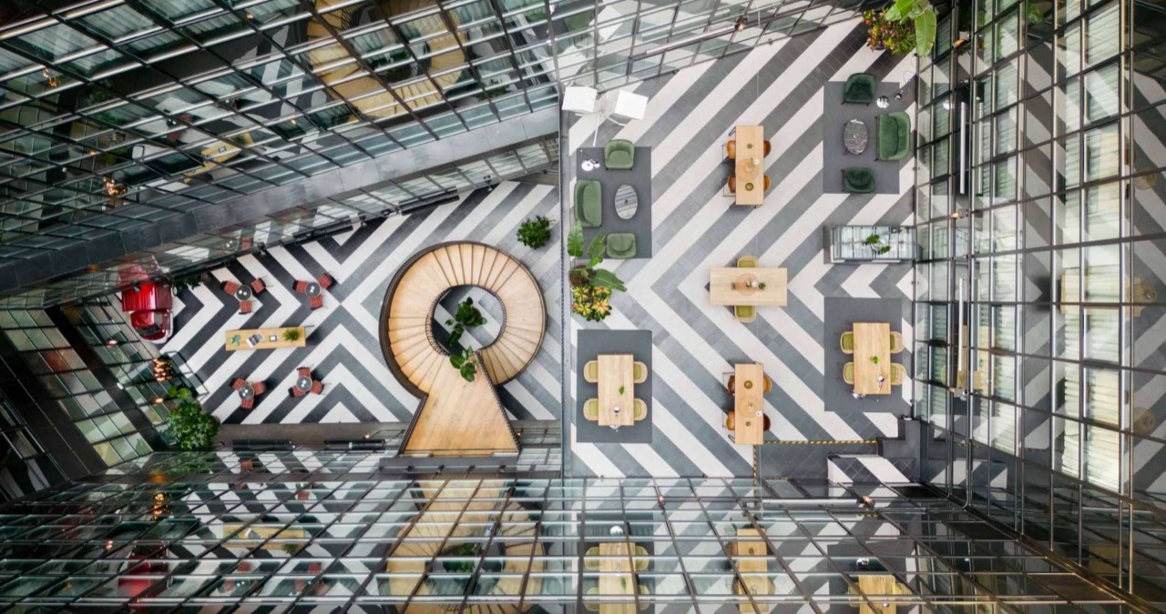 An aerial view down into the hotel's glass-walled central courtyard, showing a spiral staircase and a black-and-white geometric floor with dining tables.