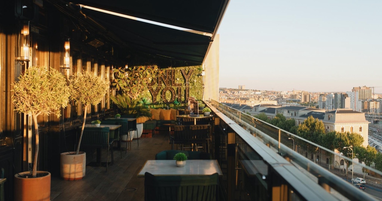 The Sép7ima rooftop terrace at sunset, with potted olive trees, lounge seating, a lit-up ONLY YOU sign, and a view over Madrid rooftops.
