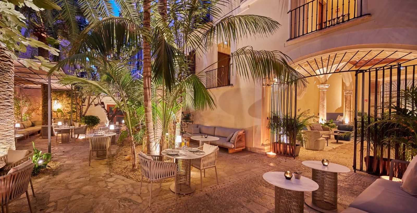 Garden courtyard with palm trees, lounge seating and café tables at dusk