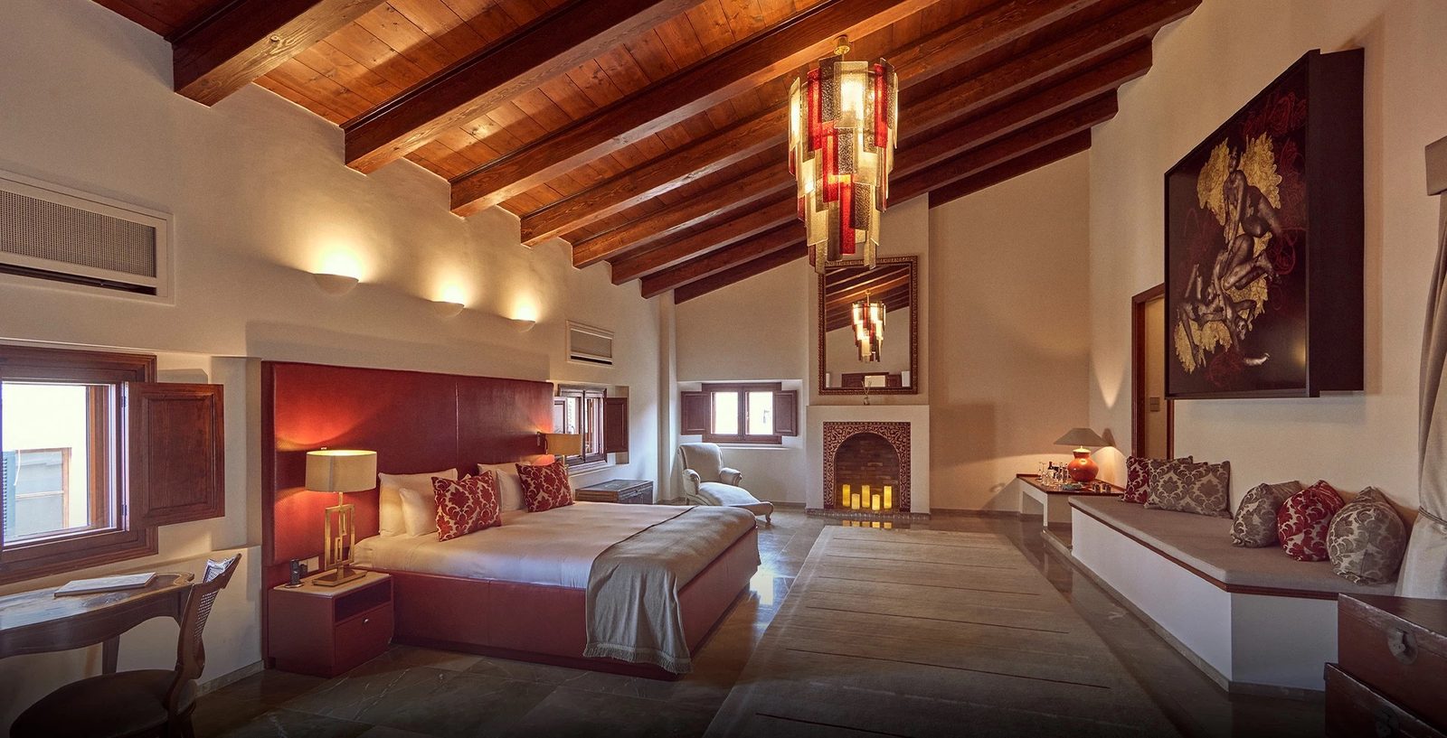 Riad Penthouse bedroom with exposed timber beams, a red headboard and a fireplace
