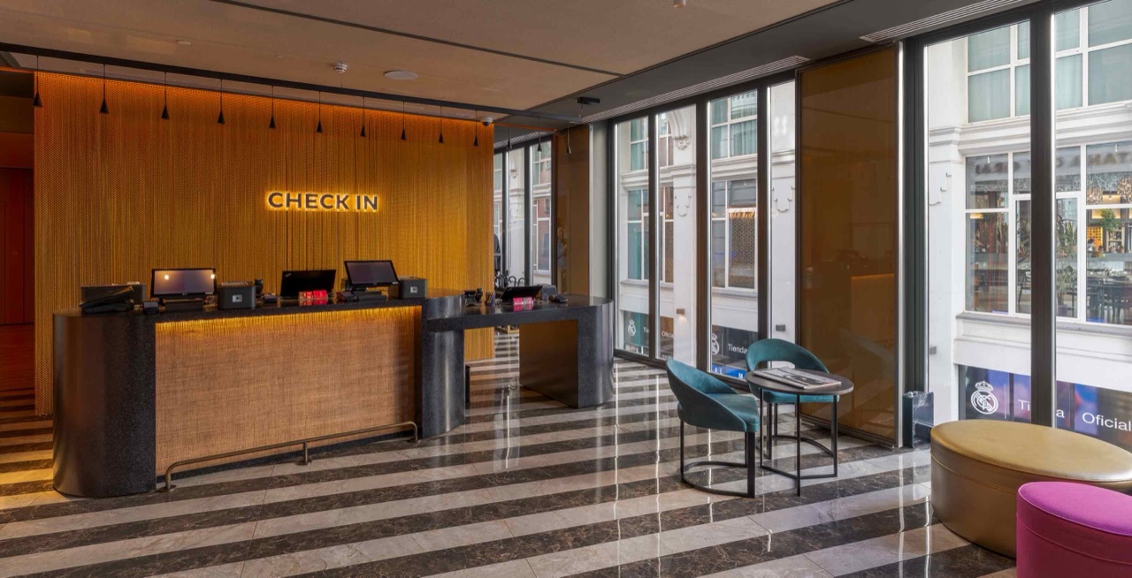 Hotel check-in desk with a woven-front counter and backlit 'CHECK IN' sign, floor-to-ceiling windows looking onto the street below.