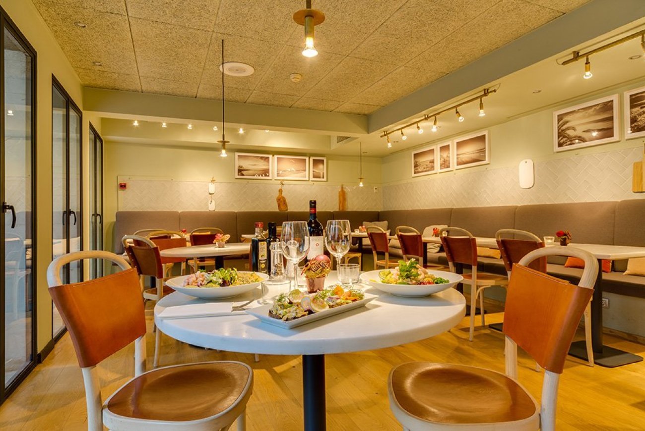 Restaurante Tres dining room with a table set with salads and tapas, banquette seating and framed coastal photography