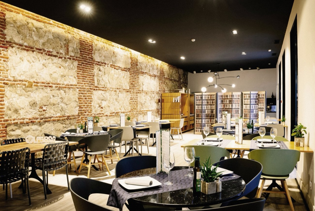 The Place To Be's indoor dining room, set tables in front of an exposed stone and brick wall, with bookshelves and hanging globe lights.