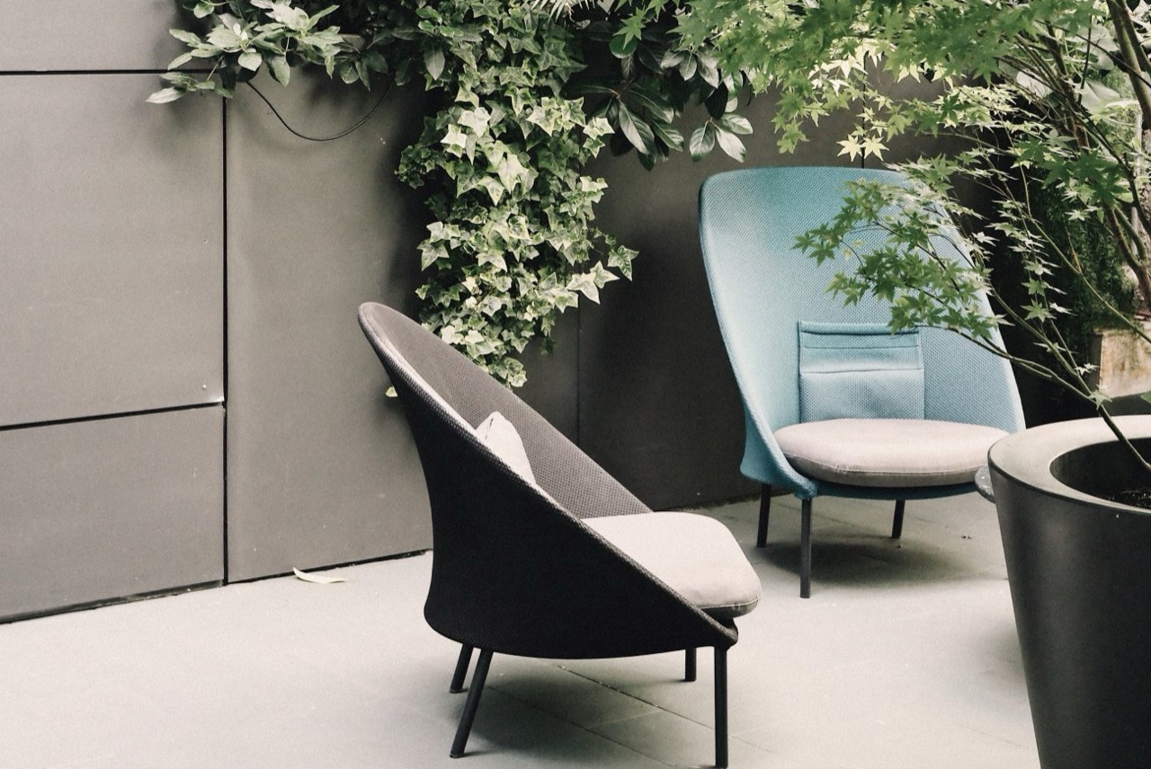 Two modern lounge chairs, one grey and one pale blue, on the hotel's plant-covered courtyard terrace.