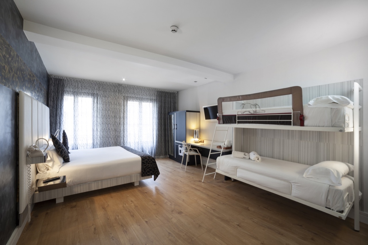 A family guest room with a double bed, a desk, a wardrobe and a bunk bed with a safety rail along the far wall.