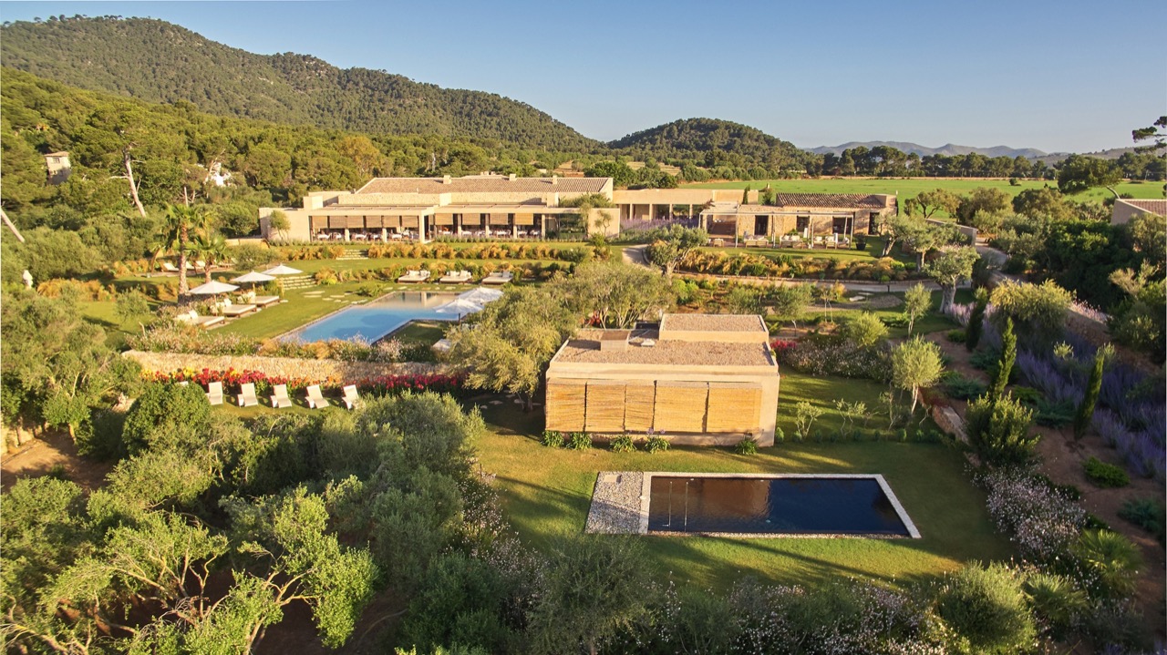 Aerial view of the hotel grounds with pools set among olive trees and hills