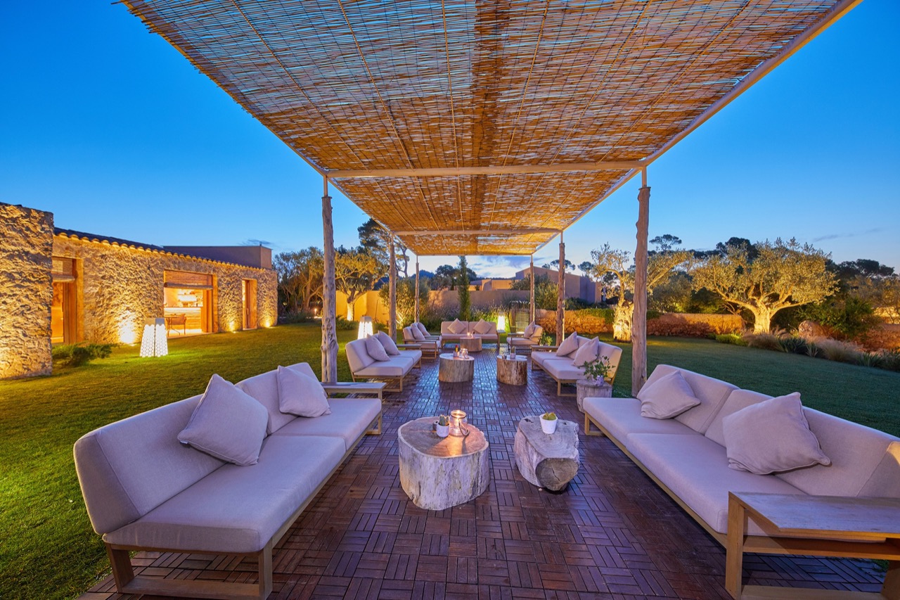 Outdoor lounge terrace with sofas under a reed pergola at dusk