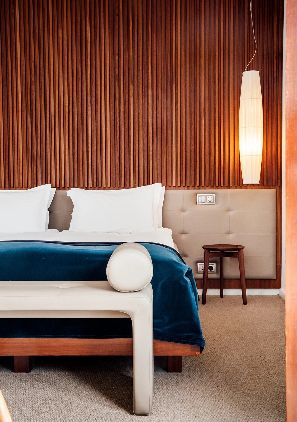 Guest room with a dark wood-slat headboard wall and a teal velvet throw on the bed