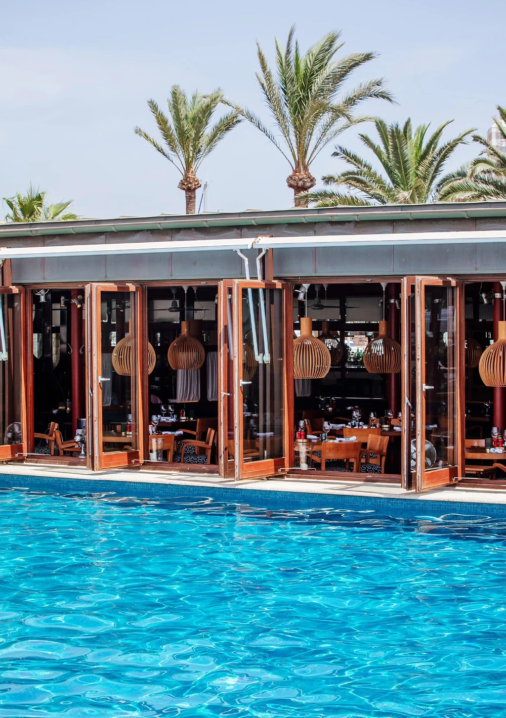The hotel's poolside restaurant pavilion with folding glass doors open to the pool, palm trees behind