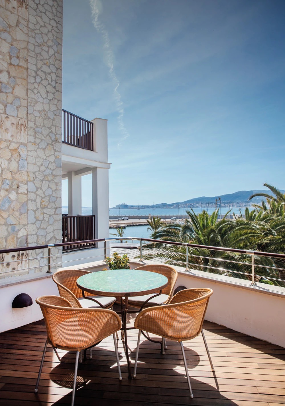 Marina View room's private terrace with wicker chairs, overlooking the harbour and palm-lined promenade