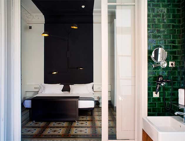 Double deluxe room at Praktik Rambla with a black headboard wall, original hydraulic tile flooring, and an en-suite bathroom sheathed in glossy emerald tile