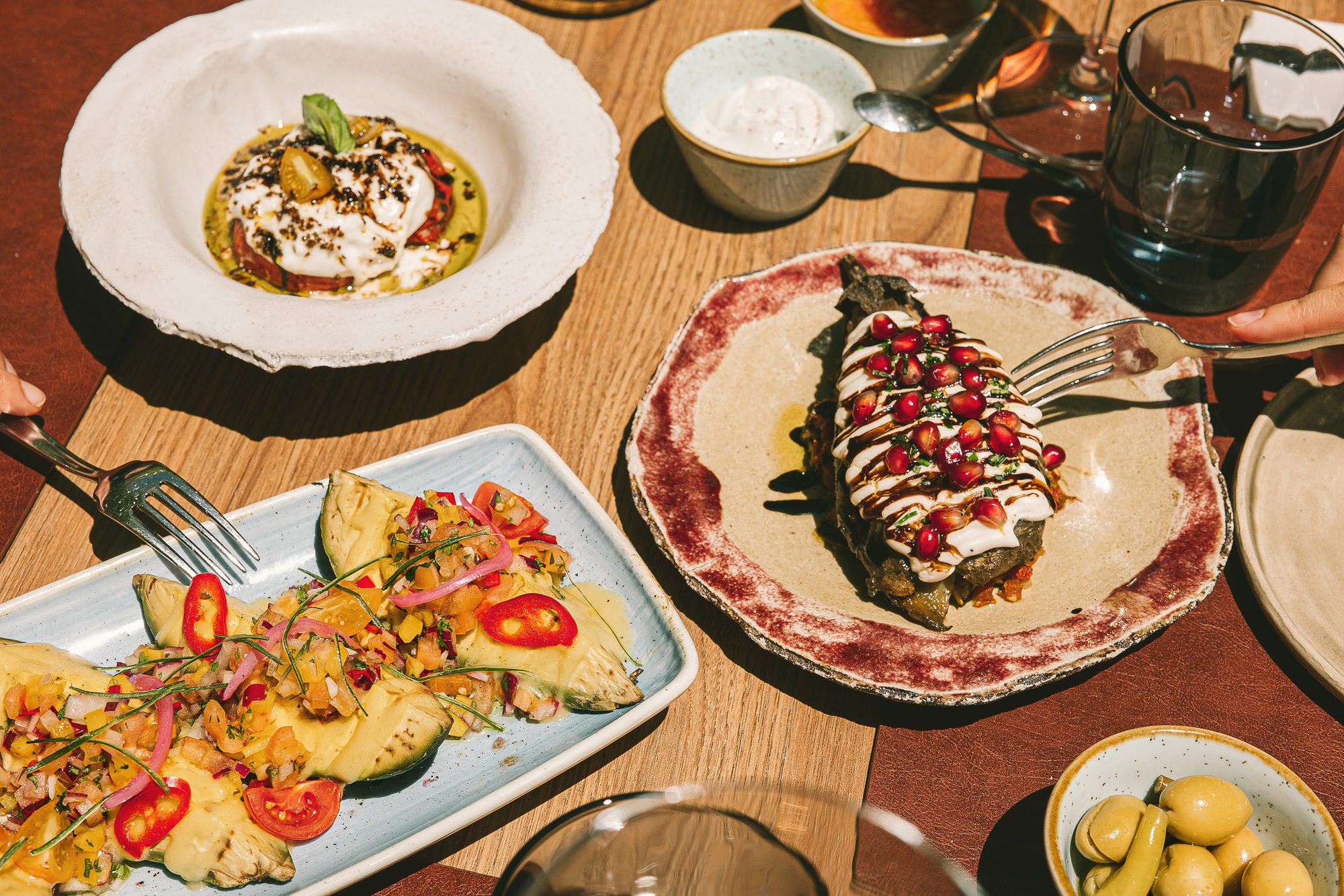 Plated dishes at Llavors, Predi Son Jaumell's restaurant, including a burrata starter, avocado tostadas and a pomegranate-topped plate on a wood table