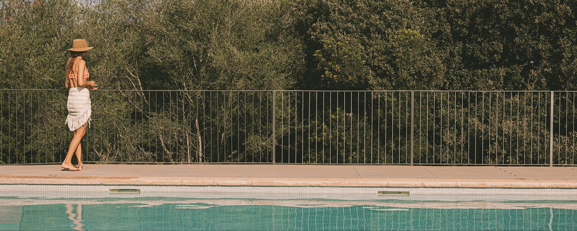 Outdoor pool at Predi Son Jaumell bordered by a tiled deck and a wooded hillside, with a guest walking along the poolside