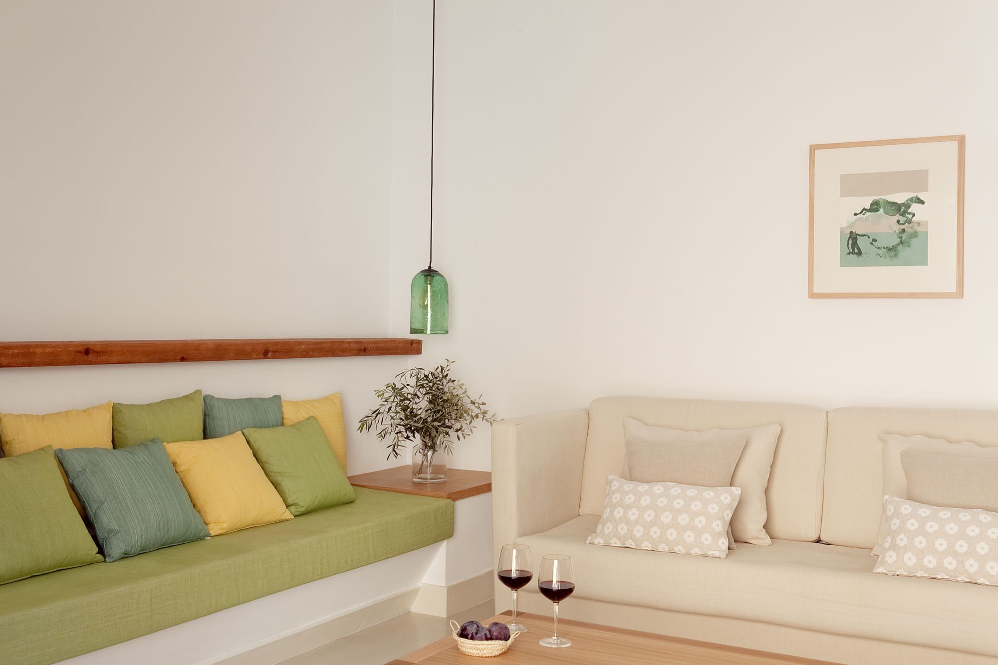 Gran Suite living area at Predi Son Jaumell with a green built-in banquette holding olive and mustard cushions, a cream sofa and a green glass pendant lamp
