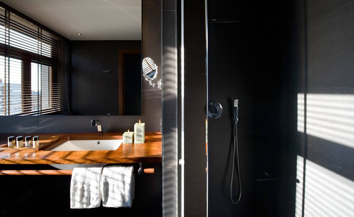 Black-tiled bathroom with a rainfall shower and a wood vanity