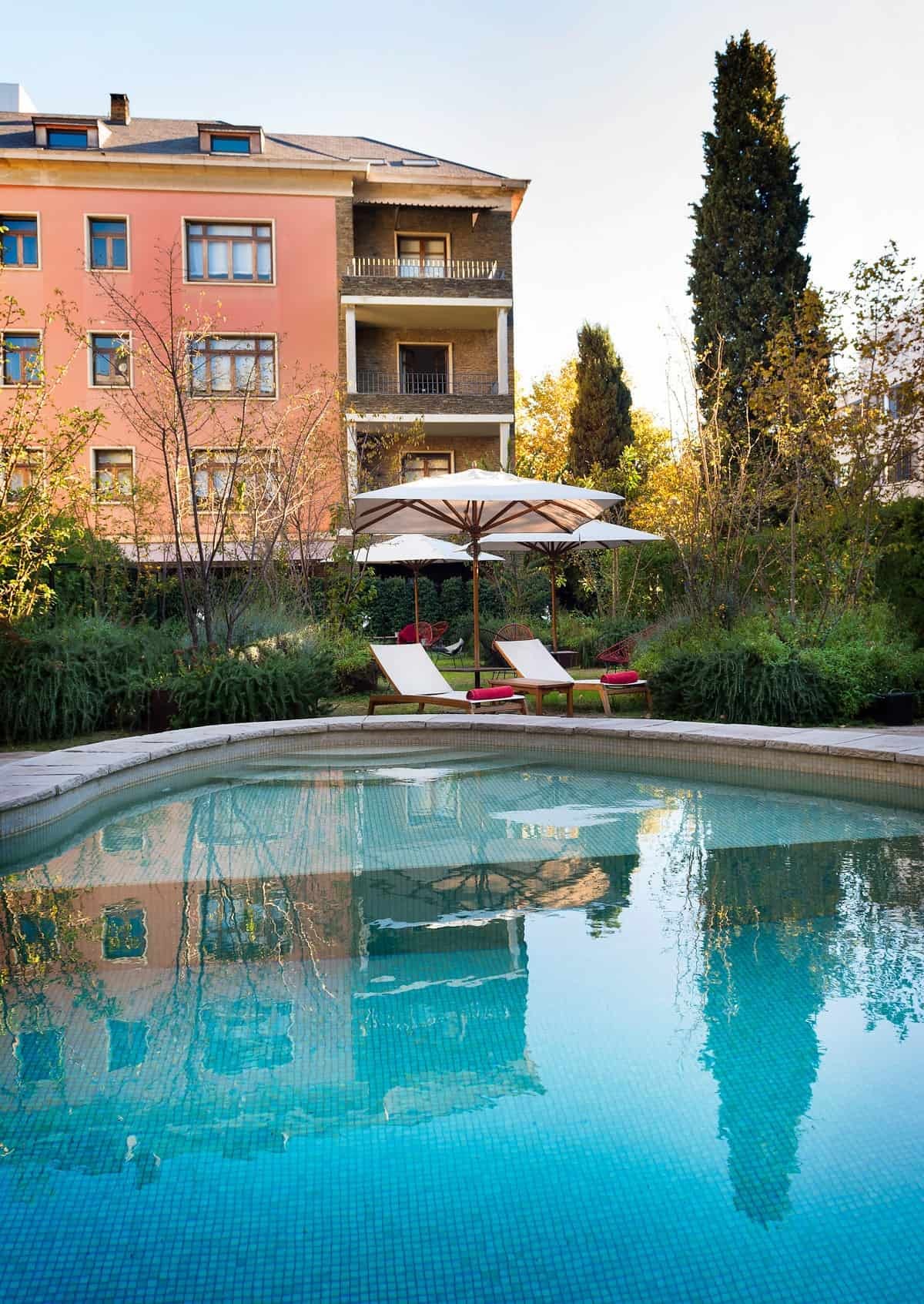 Garden pool with loungers, umbrellas and the pink hotel facade behind