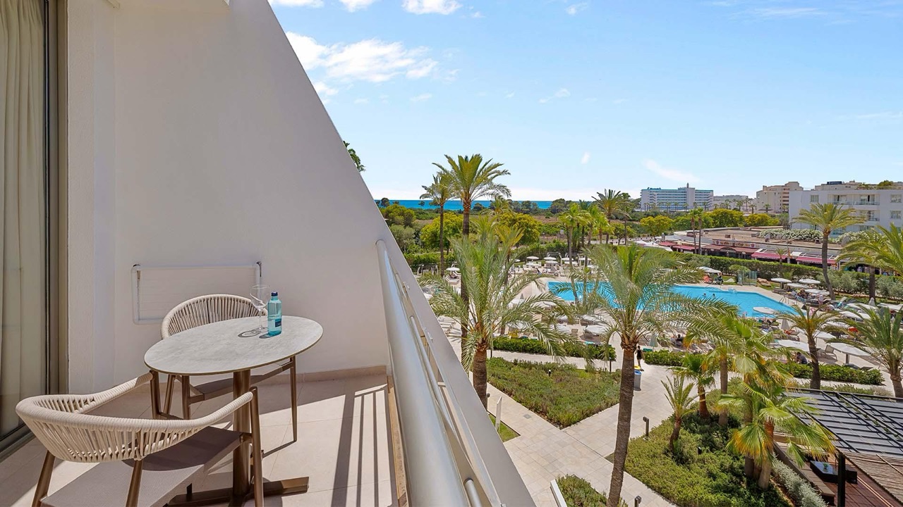 Private room balcony at Protur Sa Coma Playa Hotel & Spa with a small table and chairs looking out over the pool, gardens and the sea in the distance.