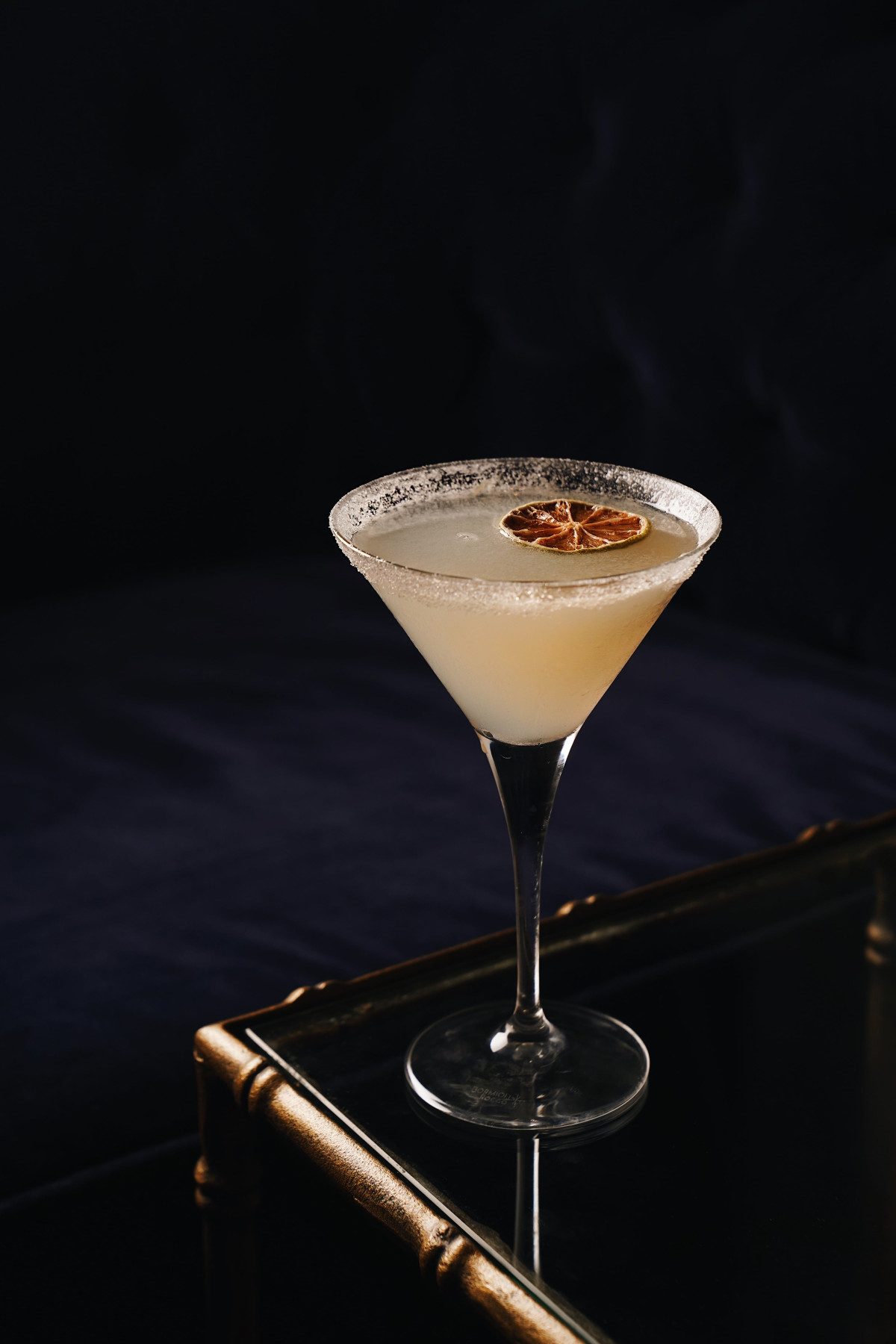 Garnished cocktail in a coupe glass on a dark tray table at the bar of Pulitzer Barcelona