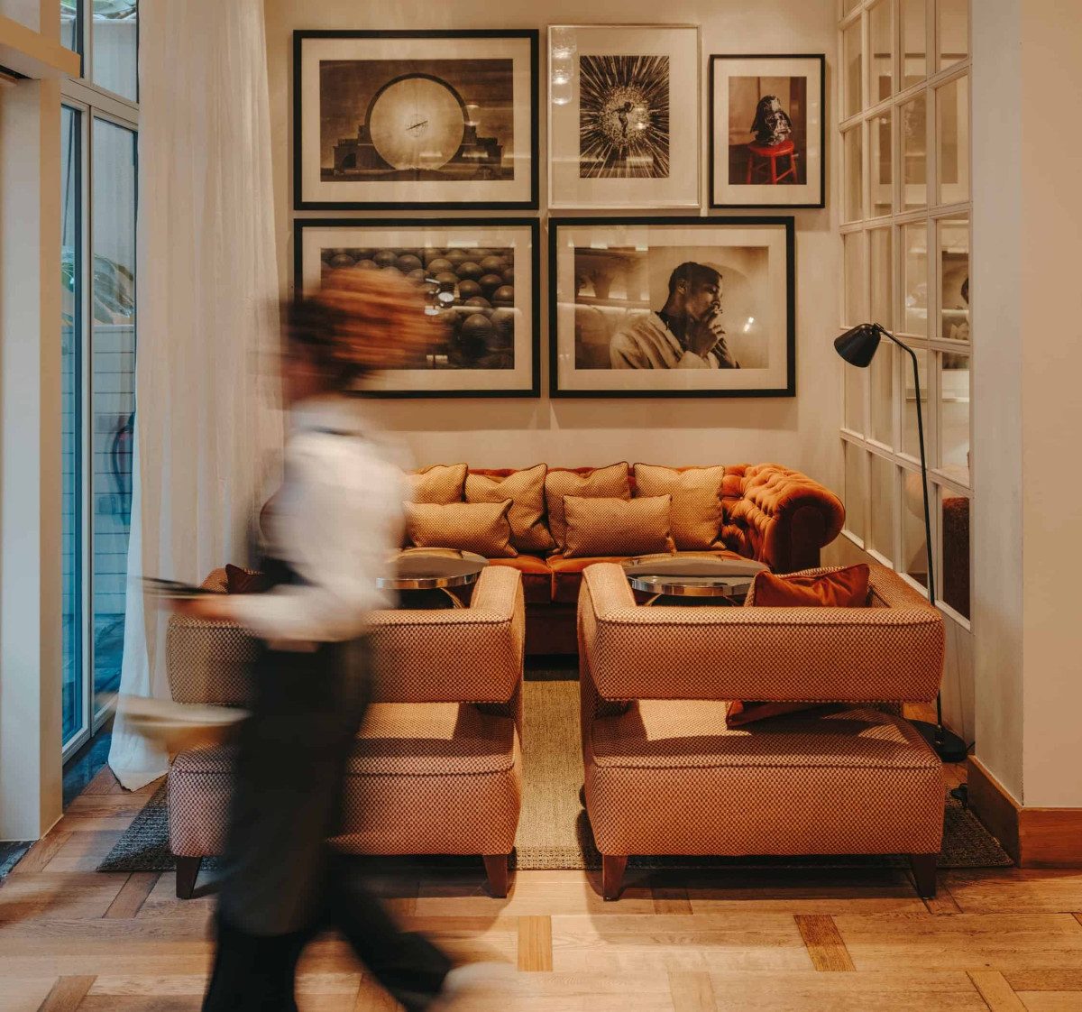 Lounge at Pulitzer Barcelona with a burnt-orange chesterfield sofa, patterned cushions, and a gallery wall of framed black-and-white photography