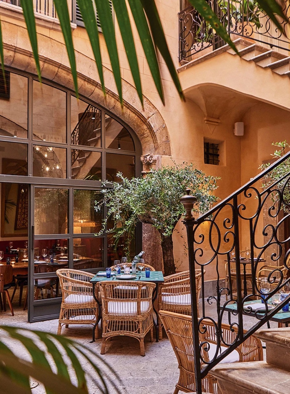 Courtyard terrace dining tables under a wrought iron staircase and olive tree