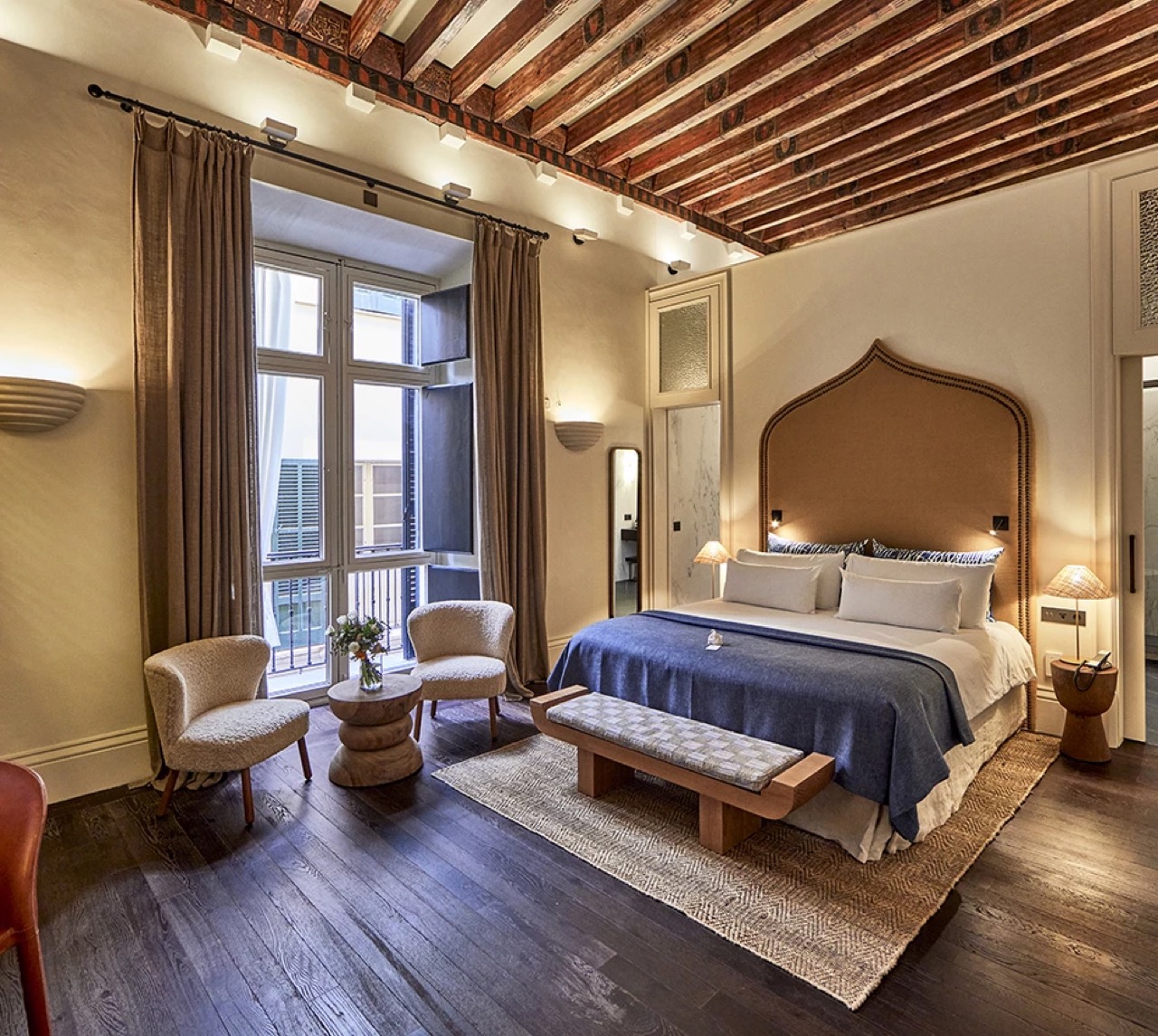 Room with an exposed painted wood beam ceiling and armchairs by the window