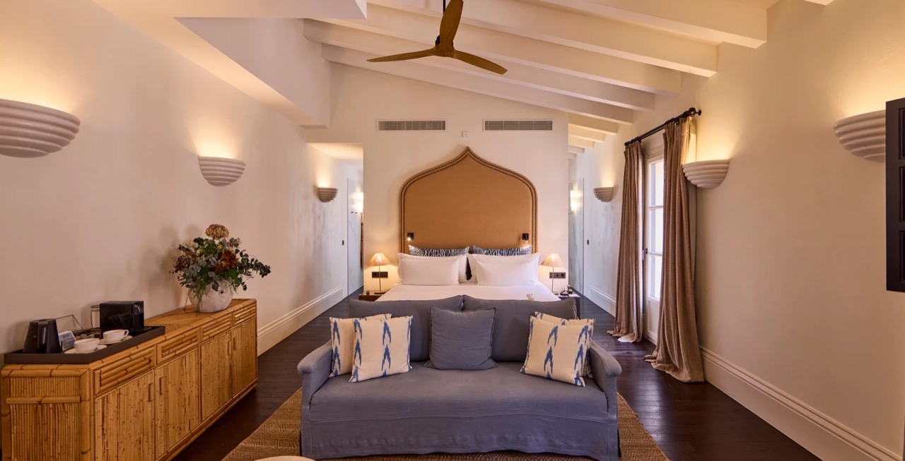 Suite bedroom with an arched cane headboard and blue sofa at the foot of the bed