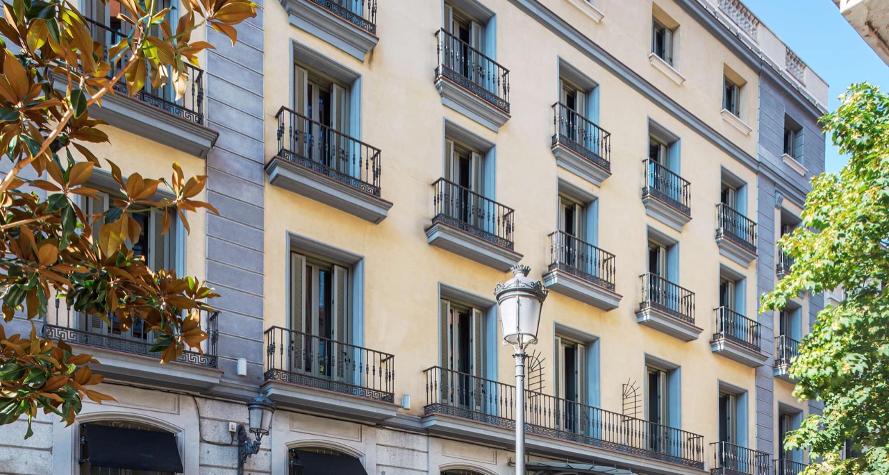 The pale yellow facade of the hotel building, with wrought-iron balconies and blue-grey window surrounds, seen from street level.