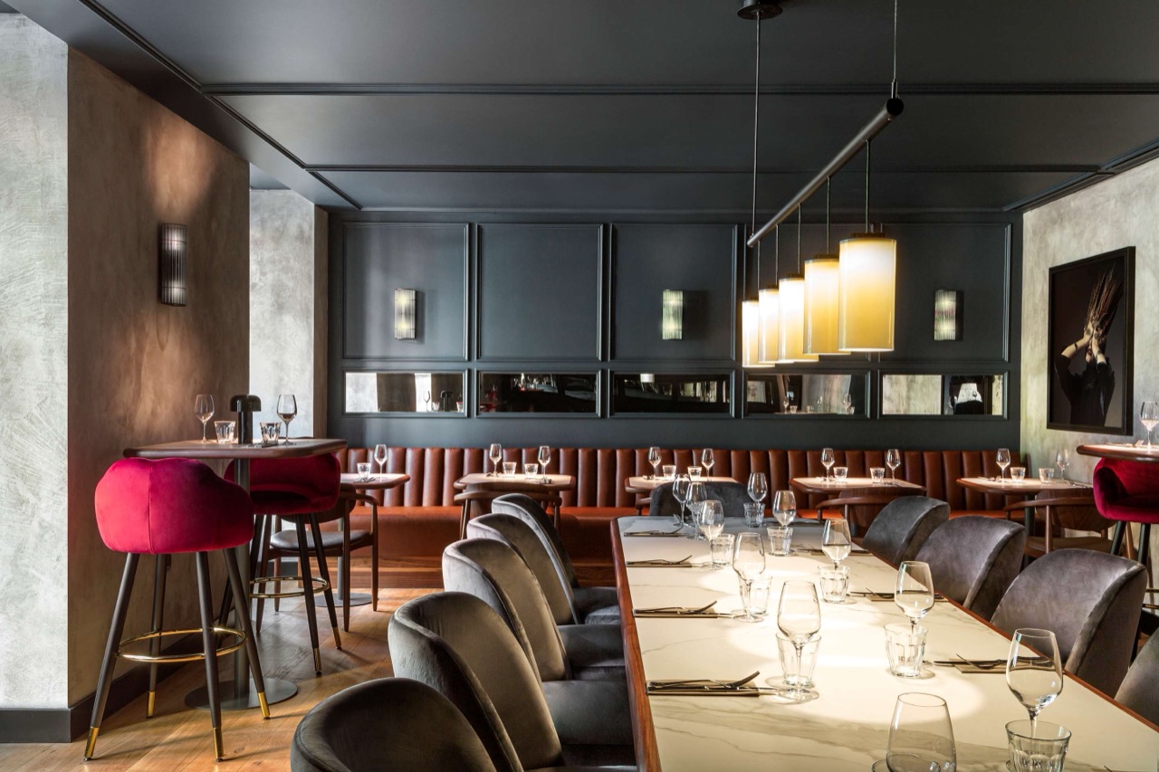 The Lona restaurant dining room, with dark wood panelling, mirrored wall panels, a long leather banquette, and pink velvet bar stools.