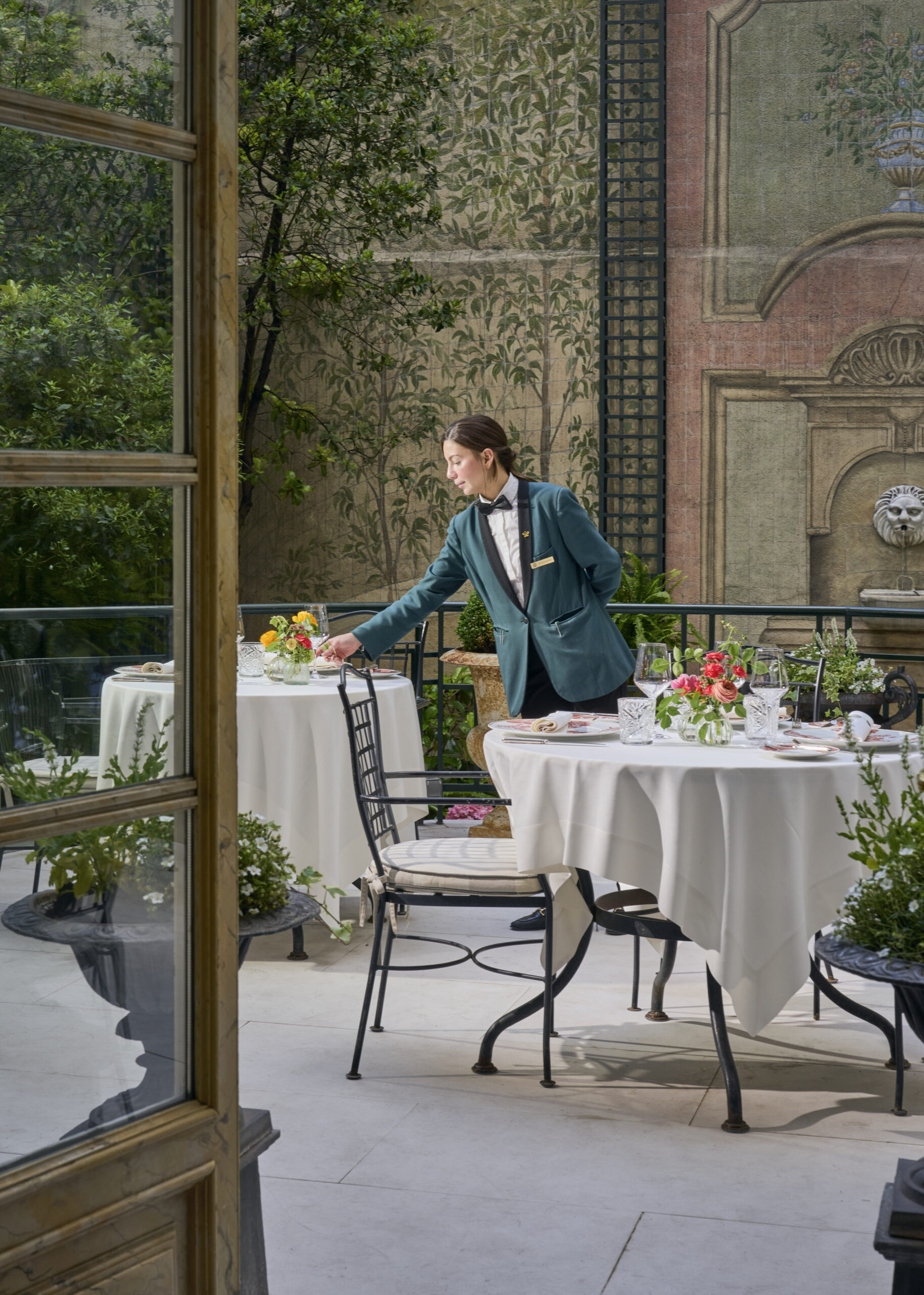 A waiter laying a table on Orfila's garden terrace, white linen and iron chairs against a painted trompe-l'oeil wall.