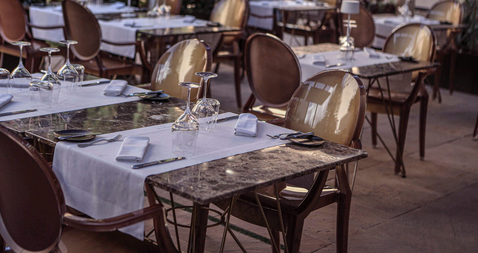 Outdoor dining terrace at Sa Creu Nova with marble-top tables, cane-back chairs and white linen runners set with wine glasses