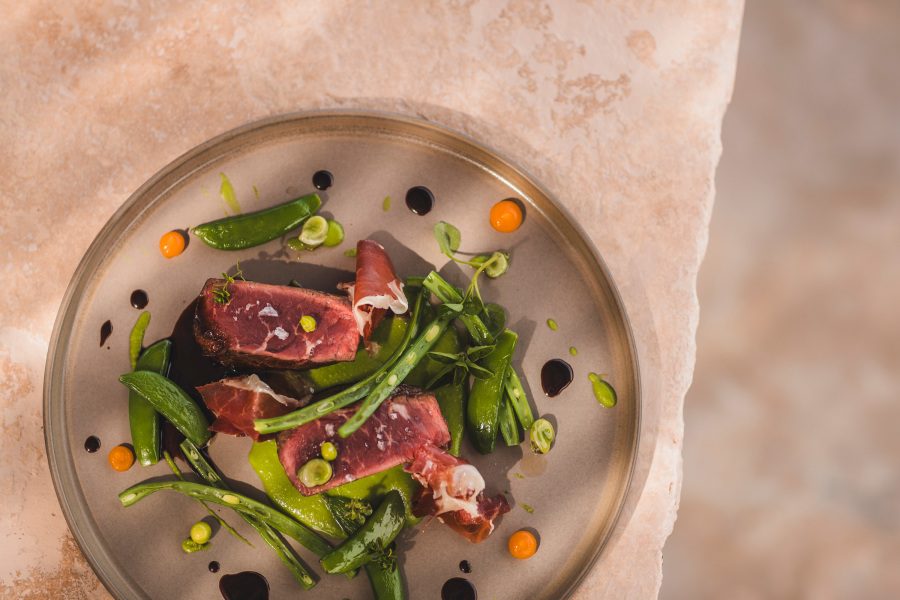 Plated dish at Es Pi, Sa Pedrissa's restaurant, with seared meat, green beans, mangetout and carrots dotted with balsamic reduction