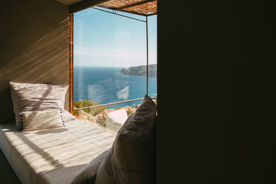 Window seat nook at Sa Pedrissa with cushions beneath a large window framing a view of the sea and a rocky coastline