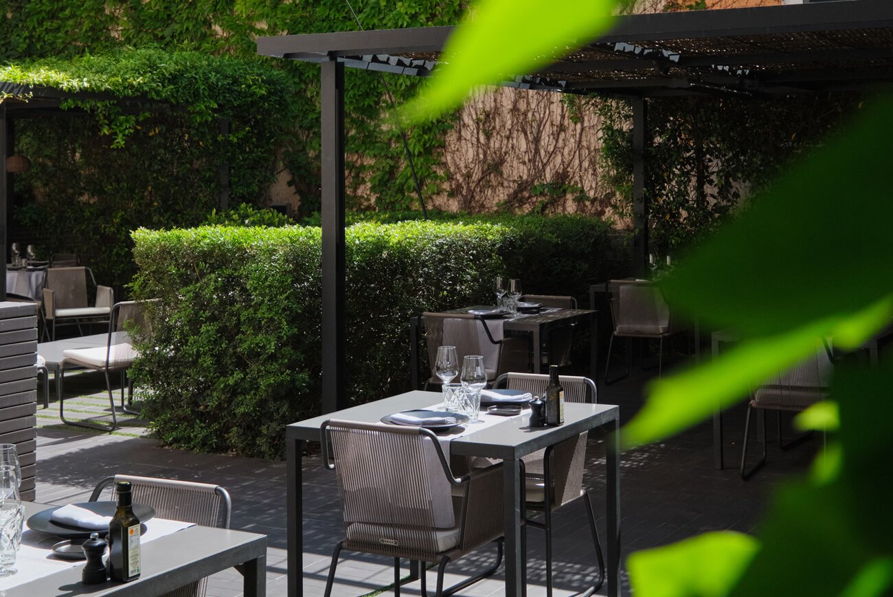 Quadrat restaurant tables set on a hedge lined garden terrace