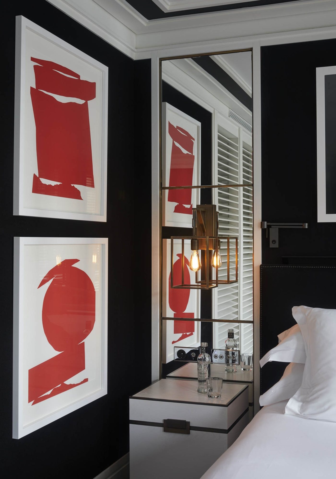 Guest room at Seventy Barcelona with black walls, red abstract art prints, a mirrored nightstand and white bedding beside plantation shutters