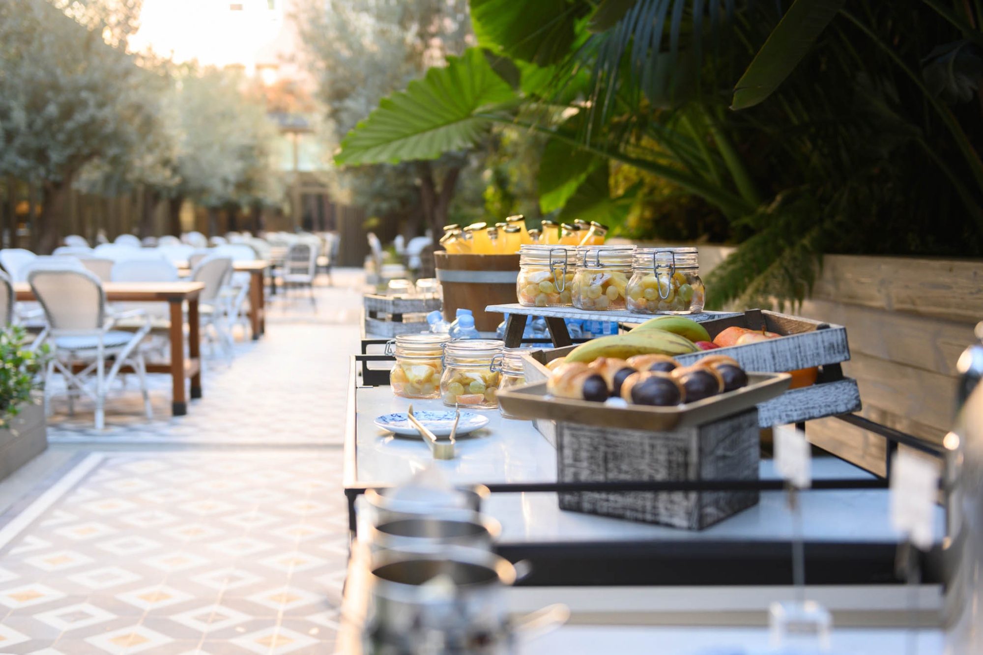 Outdoor terrace at Seventy Barcelona set up for a coffee break with jars of preserved fruit, pastries and patterned tile flooring under greenery