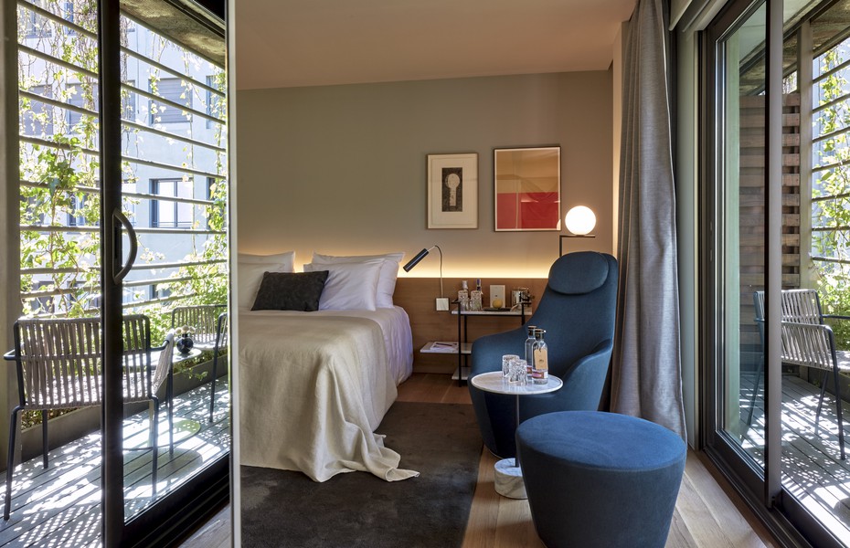 Guest room with a blue armchair and glass doors opening to a terrace