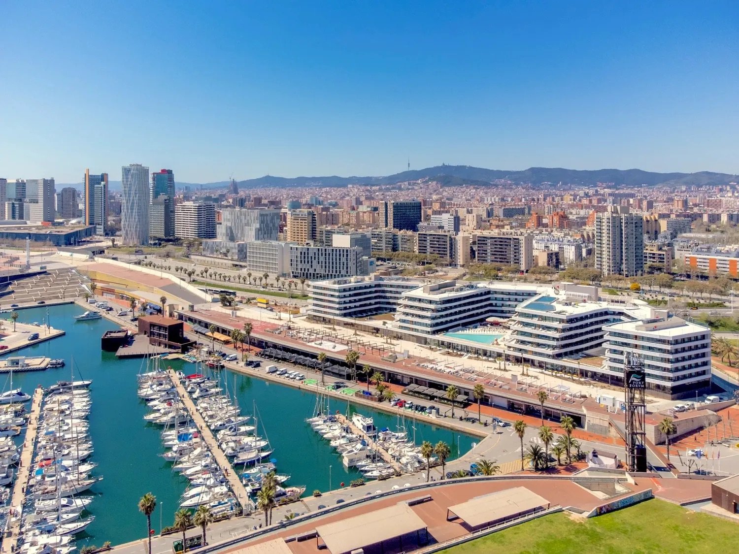 Aerial view of SLS Barcelona's terraced white buildings on the Port Fòrum marina, with moored boats and the city behind