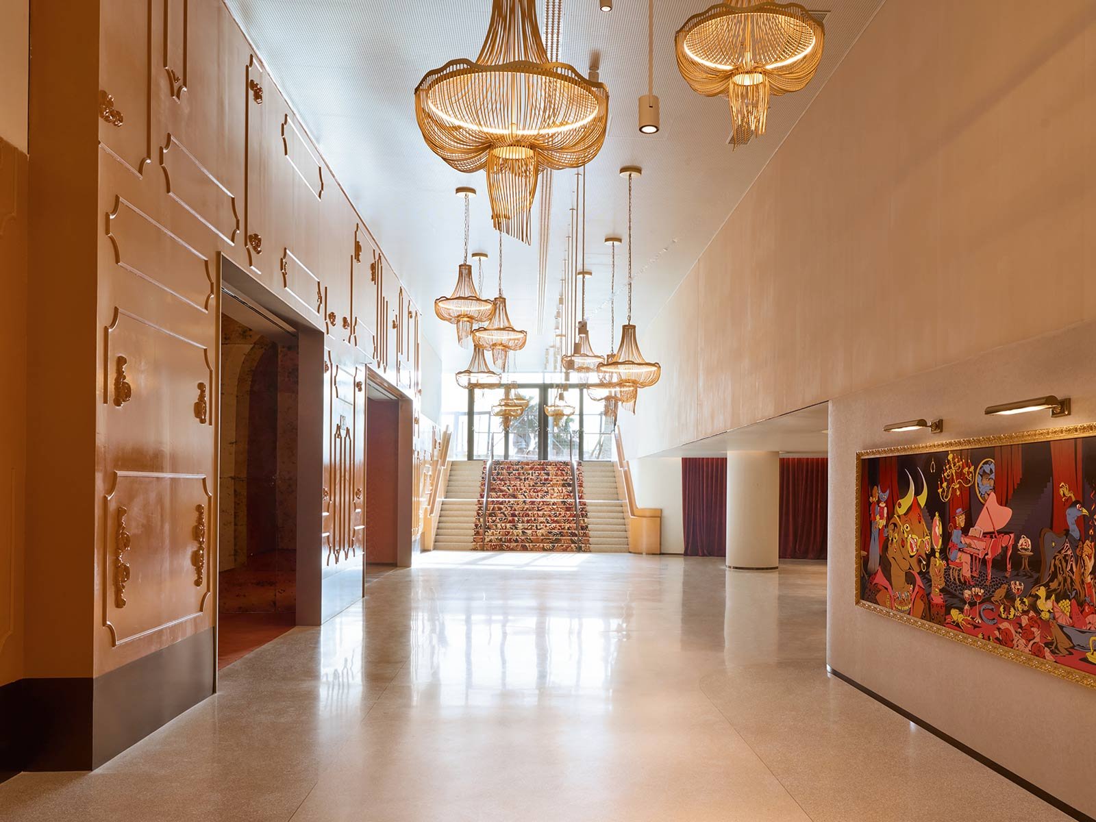 Lobby at SLS Barcelona with gold chandeliers hanging from a double-height ceiling and a colourful painting on the wall