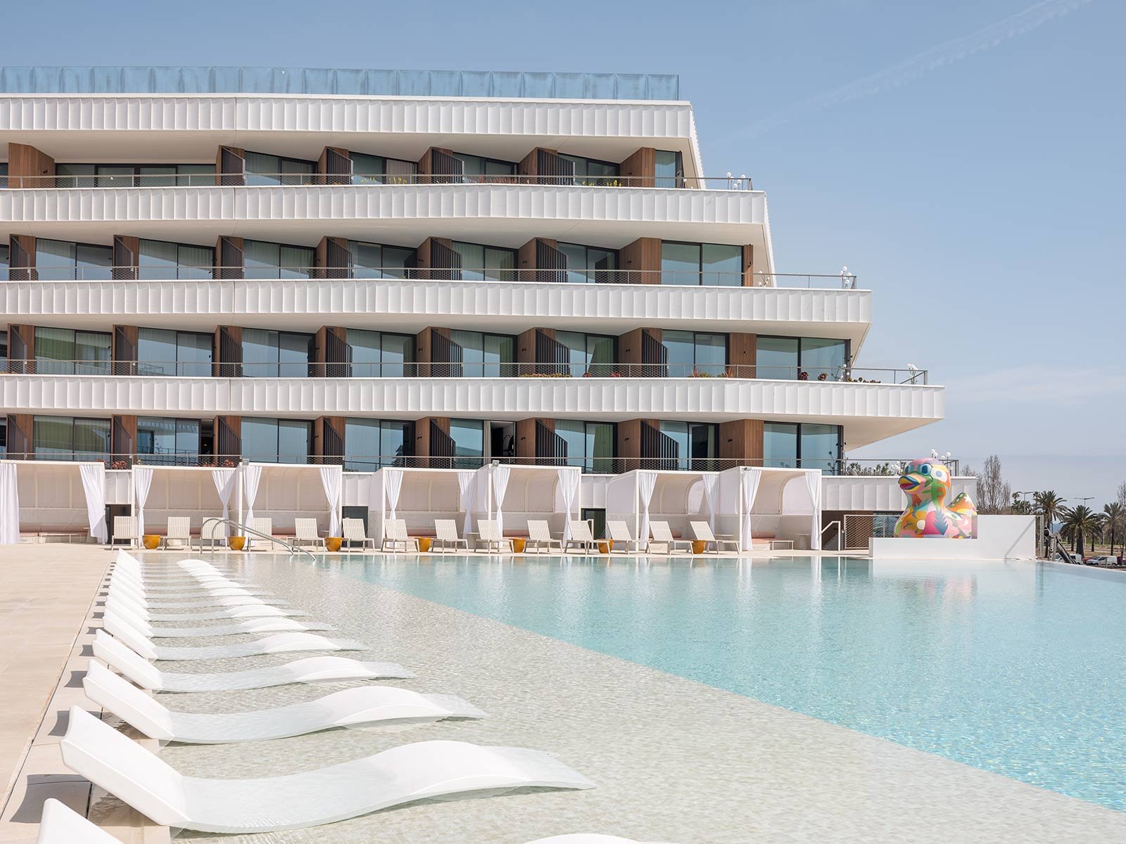 Pool at SLS Barcelona with white loungers along the water and the hotel's terraced floors behind