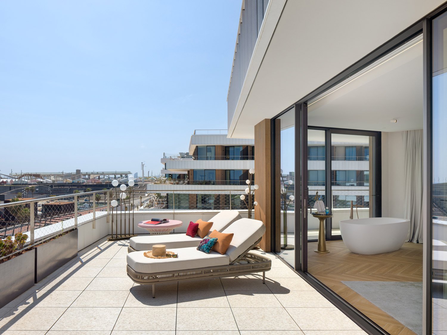 Terrace of the Luxuriate Suite at SLS Barcelona with a sun lounger, a freestanding bathtub inside and marina views