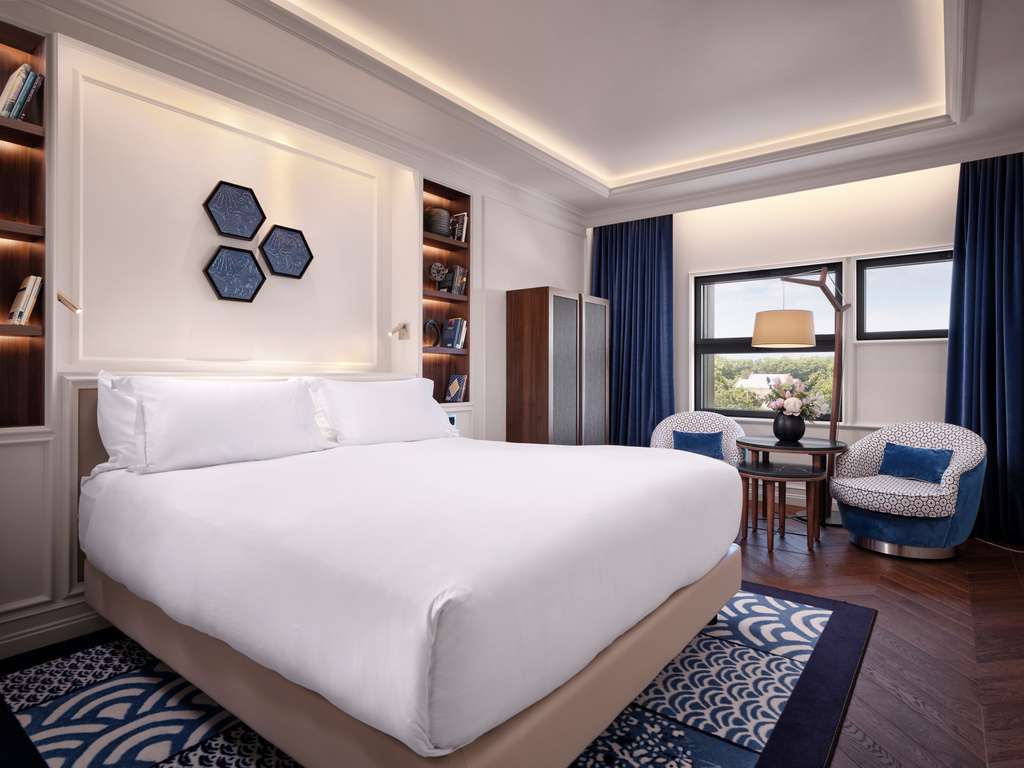 Guest room with white bedding, blue curtains and a sea-view balcony