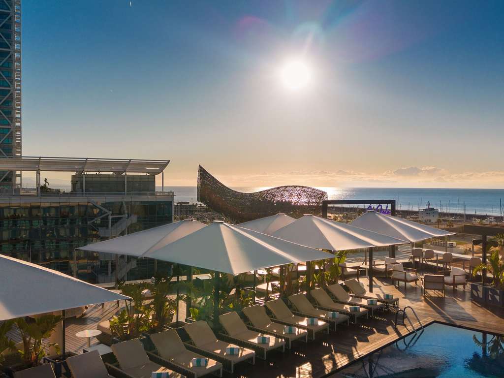 Rooftop infinity pool at sunset with the Peix sculpture and the sea behind